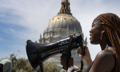 A black worker-organizer speaks into a black bullhorn at a climate action in San Francisco.